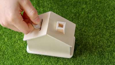 Pièce glissée dans une tirelire en forme de maison, posée sur l’herbe